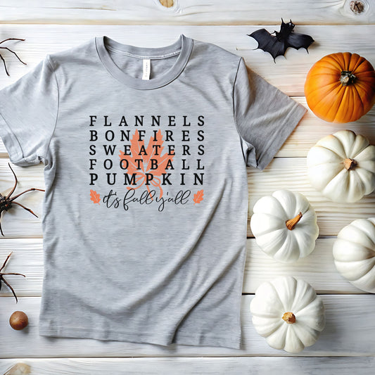 Gray short sleeve fall t-shirt with the phrase “Flannels, Bonfires, Sweaters, Football, Pumpkin, It’s Fall Y’all” in bold lettering with an orange leaf graphic behind the text.