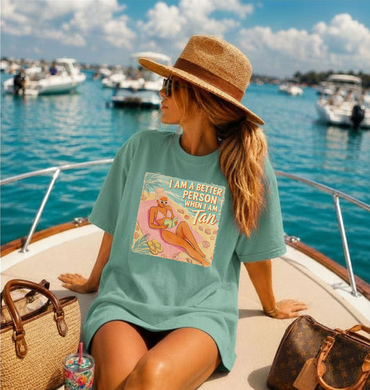 Woman sitting on a boat wearing a teal shirt with a graphic image that says im better when im tan