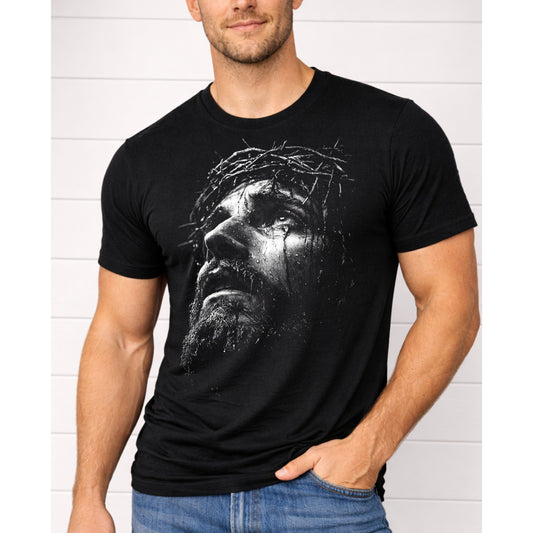 Man wearing a black t-shirt with a graphic design of a face with a crown of thorns against a white brick wall.