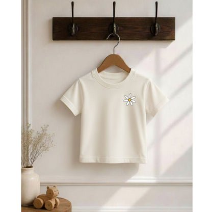 White t-shirt with a flower design on a wooden hanger against a white wall.
