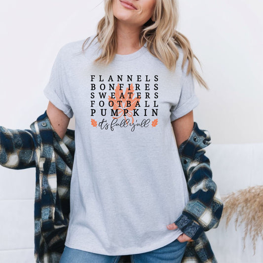 Gray short sleeve fall t-shirt with the phrase “Flannels, Bonfires, Sweaters, Football, Pumpkin, It’s Fall Y’all” in bold lettering with an orange leaf graphic behind the text.