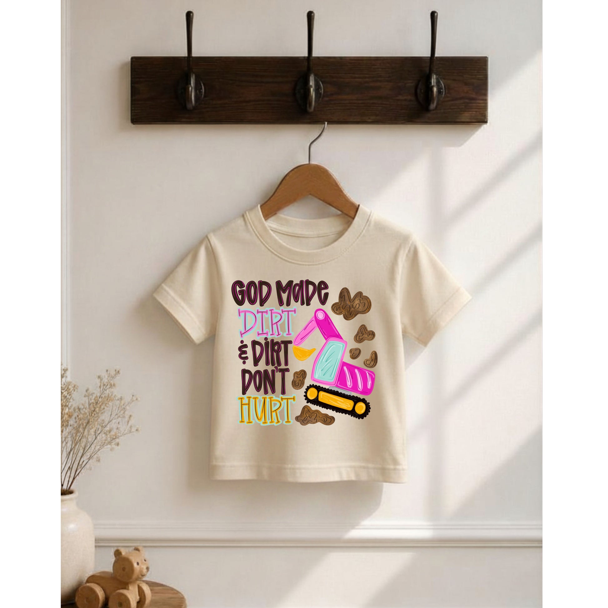 Beige t-shirt with colorful graphic and text on a wooden hanger against a white wall.