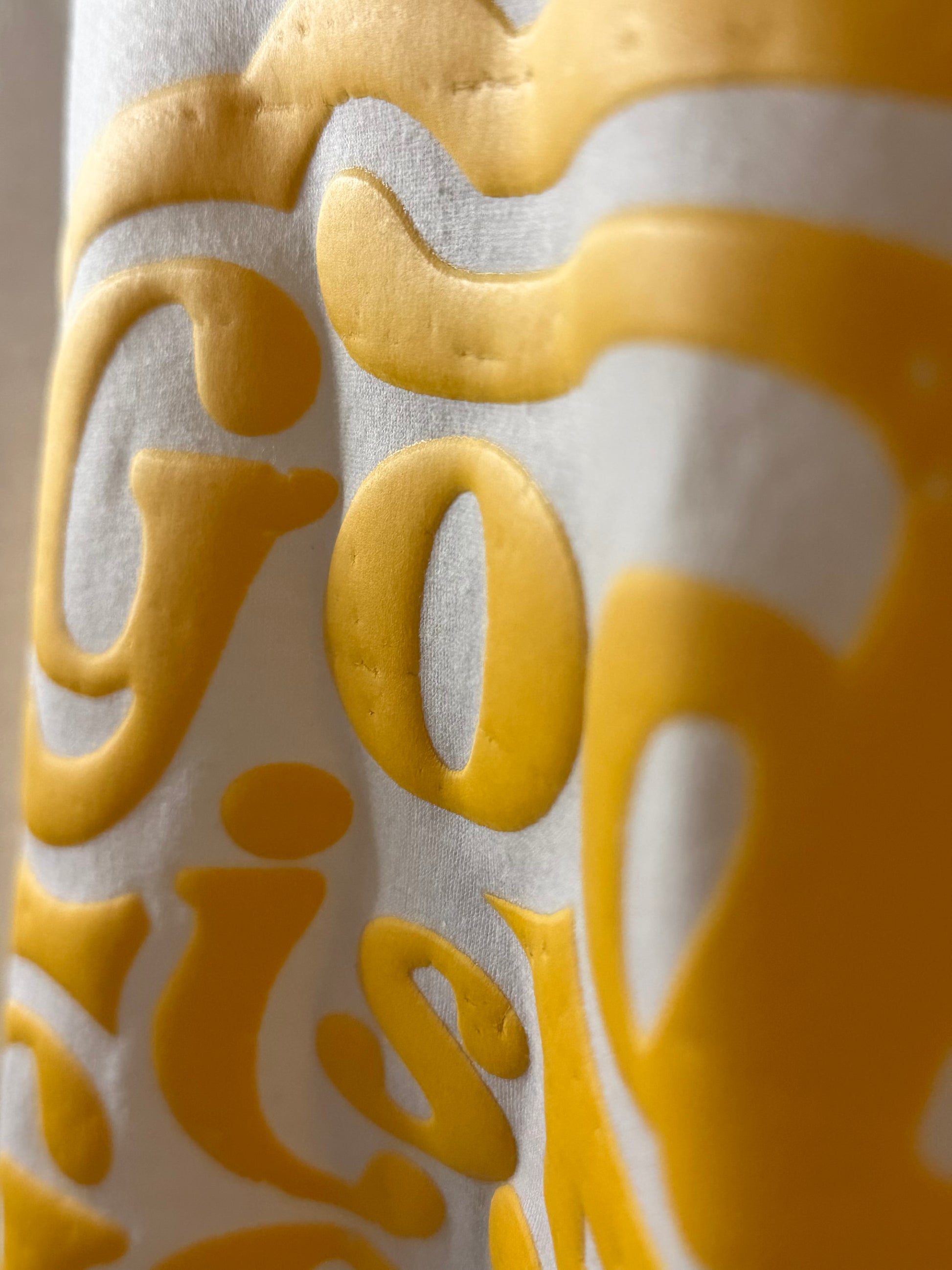 Textile with yellow puff screen print letters on a white background