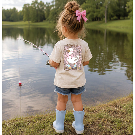 Child fishing by a lake wearing a shirt with a goose design.