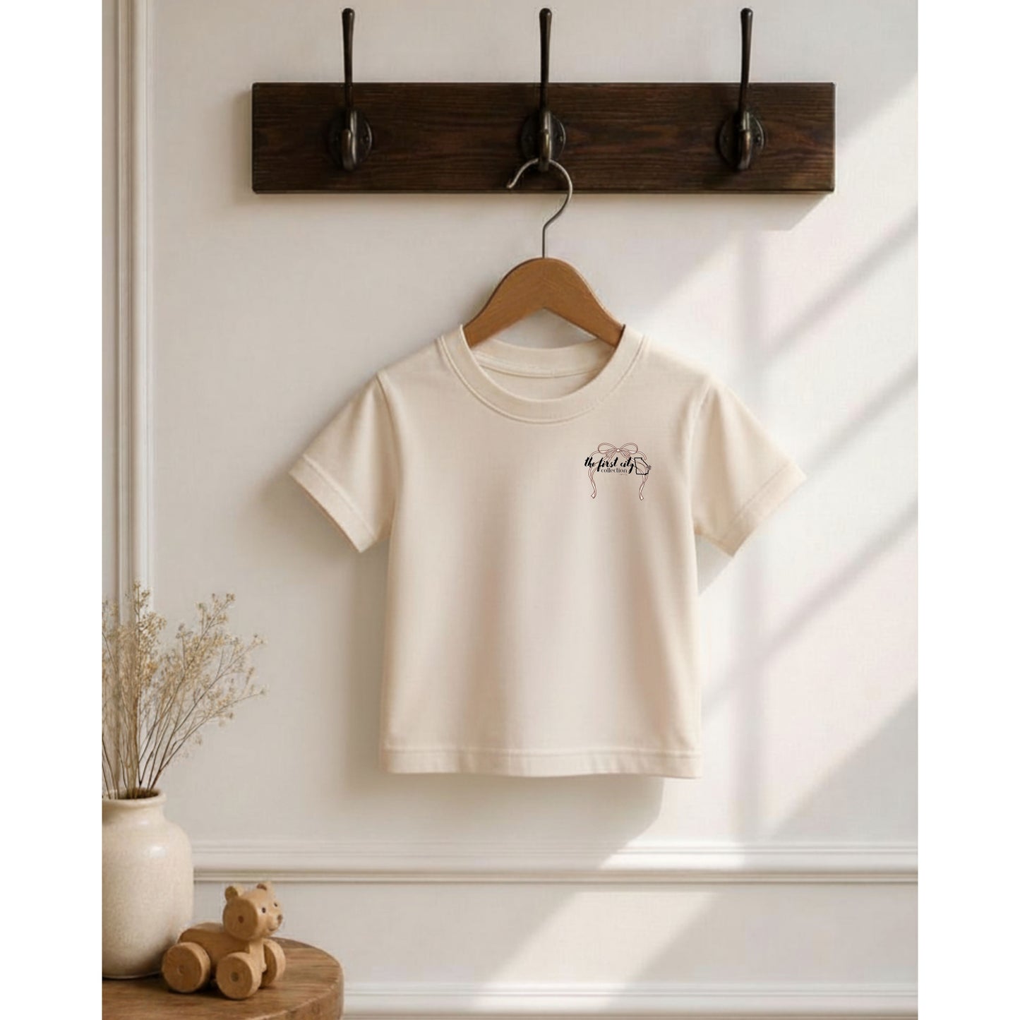 White t-shirt with a small design on a wooden hanger against a light wall.