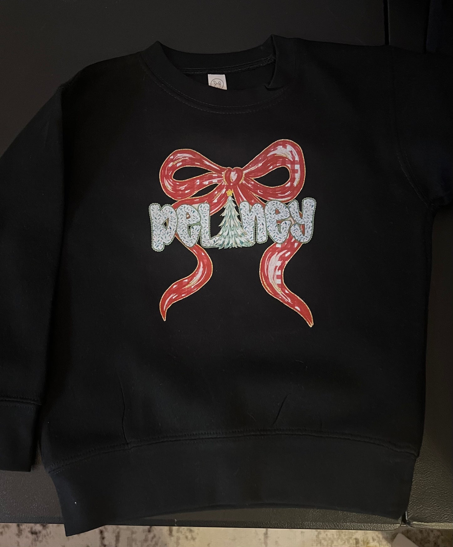 Black sweatshirt with a red bow and 'Delaney' text design on a dark background