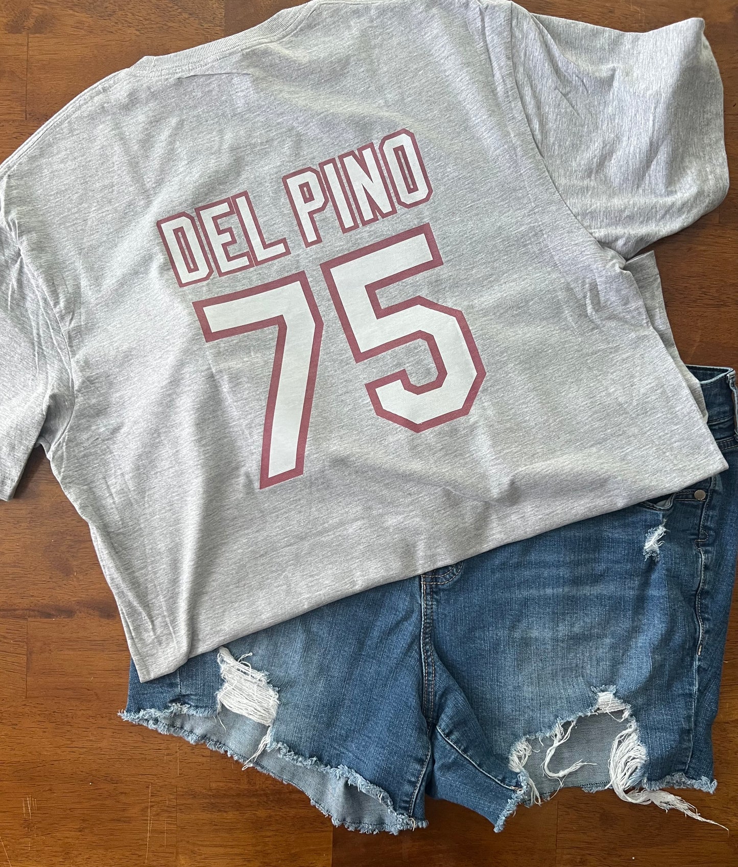 Gray t-shirt with 'DEL PINO 75' text and denim shorts on a wooden surface