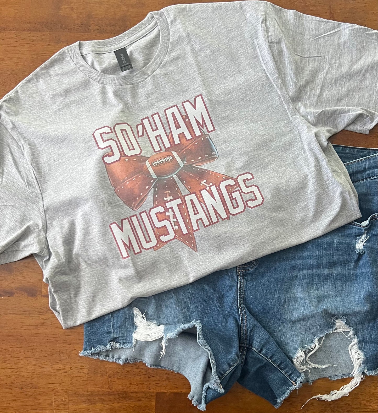 Gray t-shirt with 'So'Ham Mustangs' design on a wooden surface with denim shorts.
