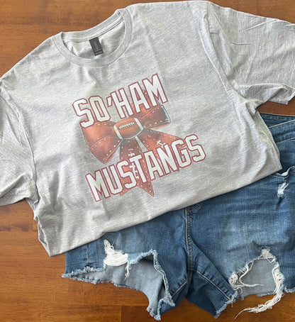 Gray t-shirt with 'So'Ham Mustangs' design on a wooden surface with denim shorts.