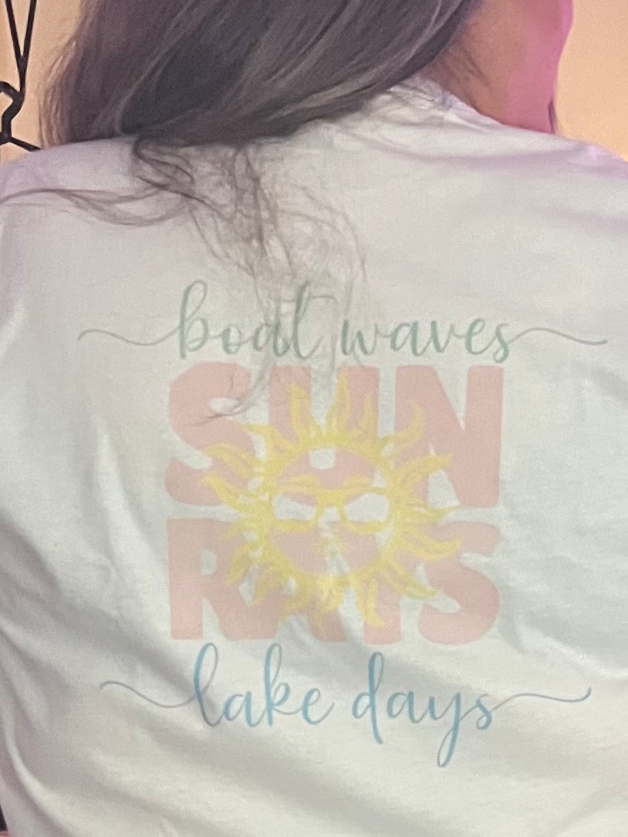 White t-shirt with 'boat waves sun rose lake days' text and sun graphic on a person's back.
