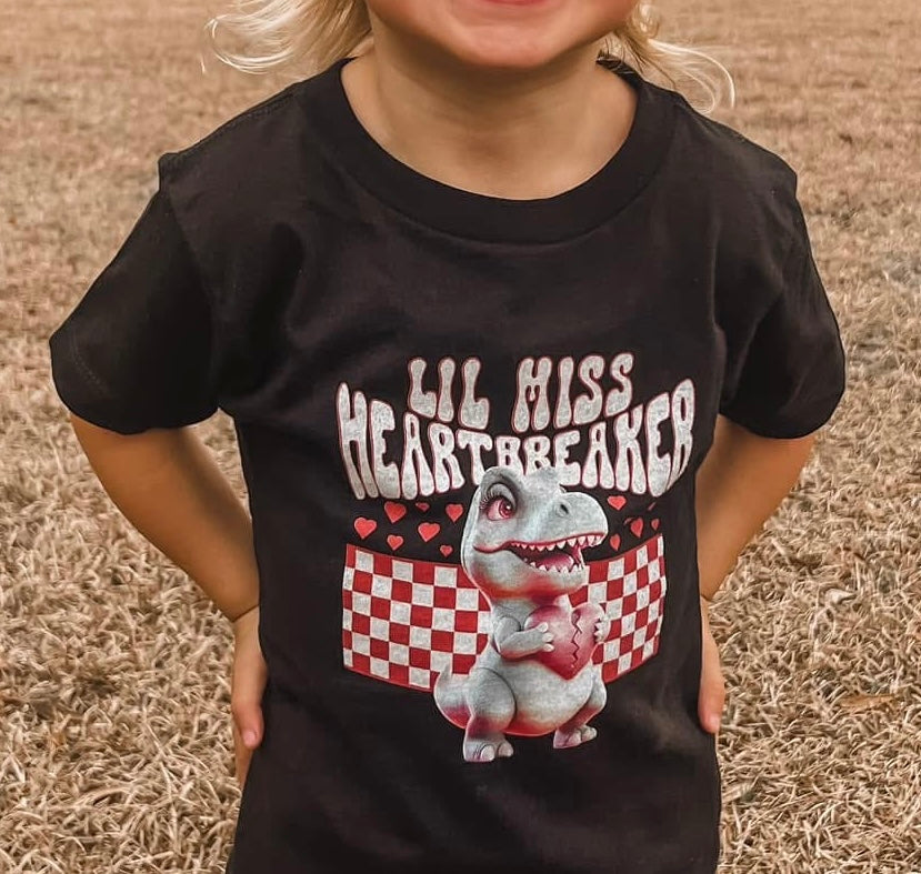 Child wearing a black t-shirt with a dinosaur graphic and text on a grassy background