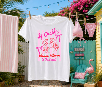 White graphic T-shirt hanging on a backyard clothesline featuring a pink "If Crabby, Please Return to the Beach" crab design with coastal décor, beach cottage, and tropical summer setting.