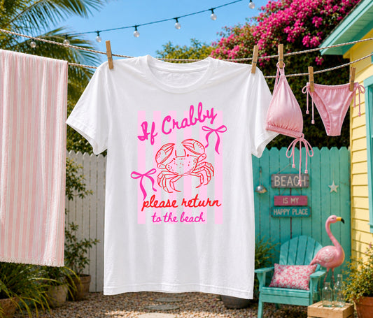 White graphic T-shirt hanging on a backyard clothesline featuring a pink "If Crabby, Please Return to the Beach" crab design with coastal décor, beach cottage, and tropical summer setting.