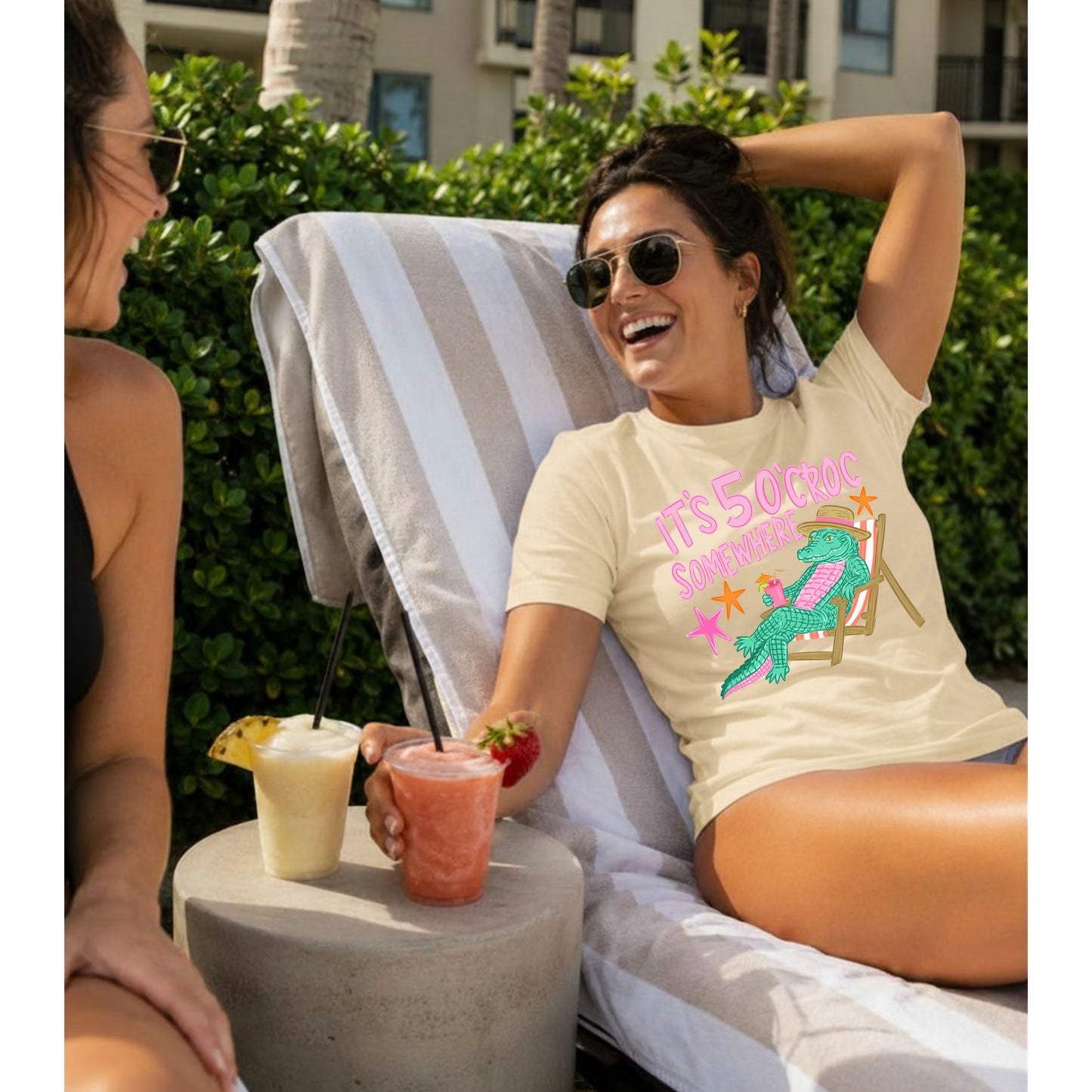 Woman relaxing poolside in a cream graphic T-shirt featuring the colorful "It's 5 O'Croc Somewhere" alligator design while enjoying frozen drinks on a sunny summer afternoon.
