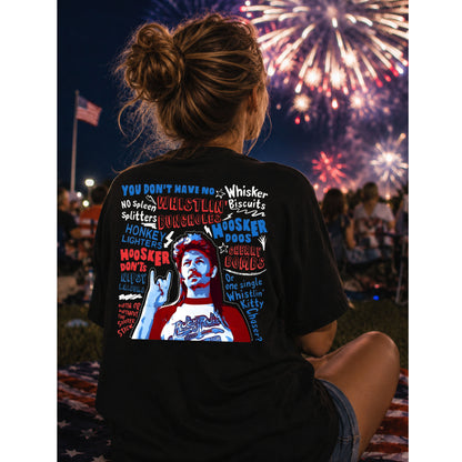 Person wearing a black t-shirt with colorful graphics and text, sitting in front of fireworks.
