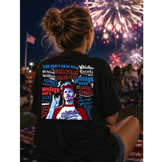Person wearing a black t-shirt with colorful graphics and text, sitting in front of fireworks.