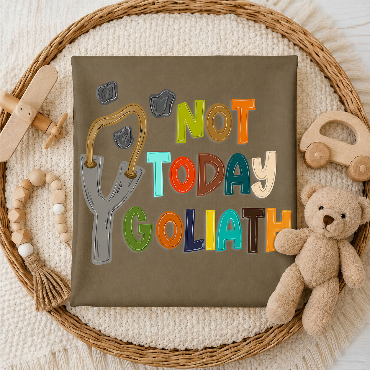 T-shirt with 'Not Today Goliath' text surrounded by toys on a textured surface