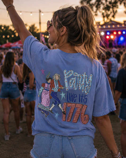 Person wearing a blue t-shirt with 'Party Like It's 1776' design at a festival.