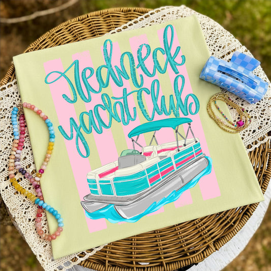 Folded butter yellow graphic T-shirt featuring the colorful "Redneck Yacht Club" pontoon boat design, styled on a woven tray with pastel beaded bracelets, layered jewelry, and a blue checkered hair clip.