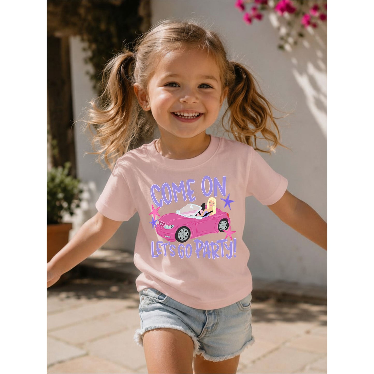 Child wearing a pink t-shirt with a graphic and text, standing outdoors.