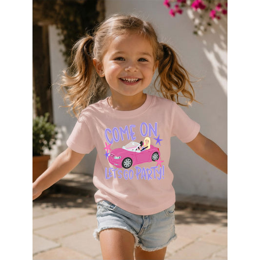 Child wearing a pink t-shirt with a graphic and text, standing outdoors.