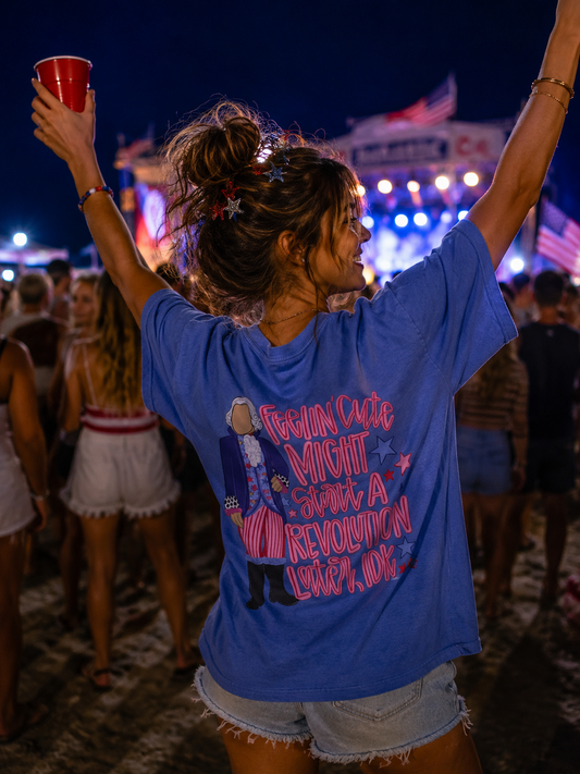 Woman at a concert or festival wearing a blue t-shirt with text, holding a red cup.